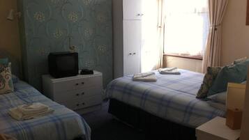 Een slaapkamer met twee bedden, een garderobe, een televisie en een raam met gordijnen.