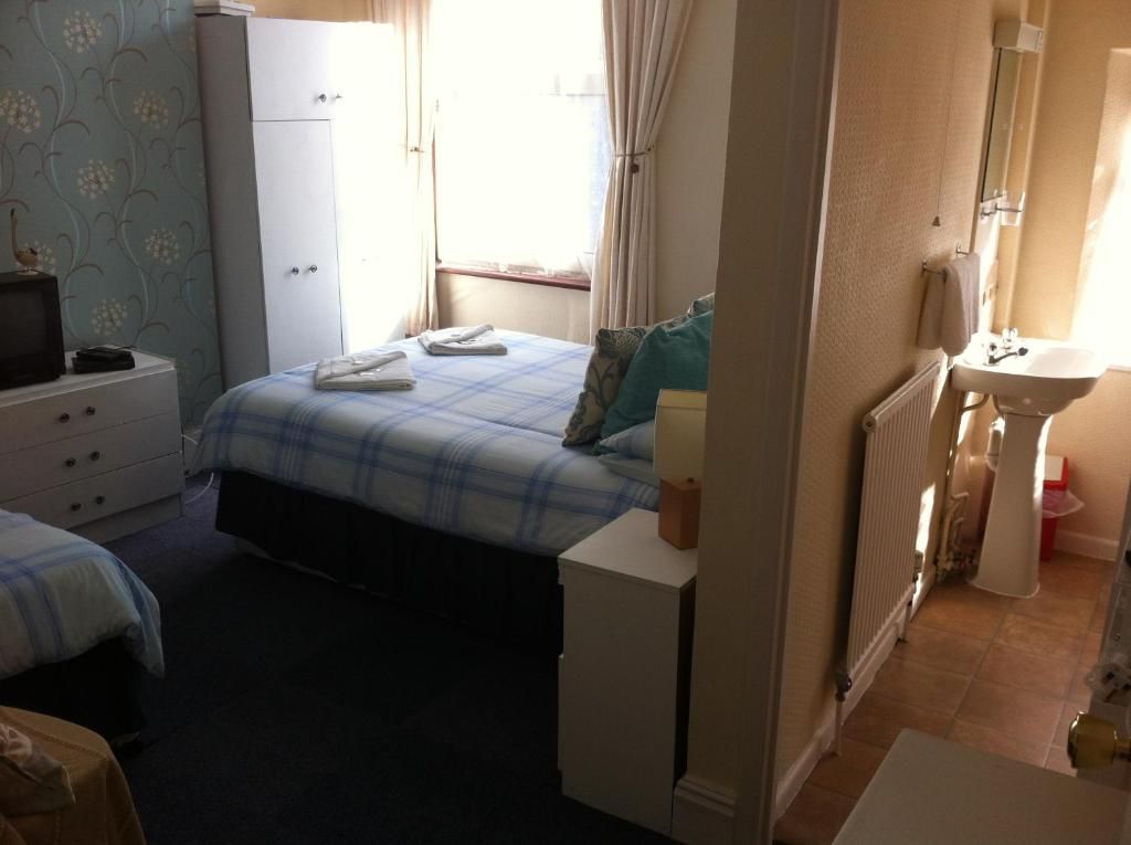 A bedroom with a bed, a dresser, a bedside table, and a window with curtains.