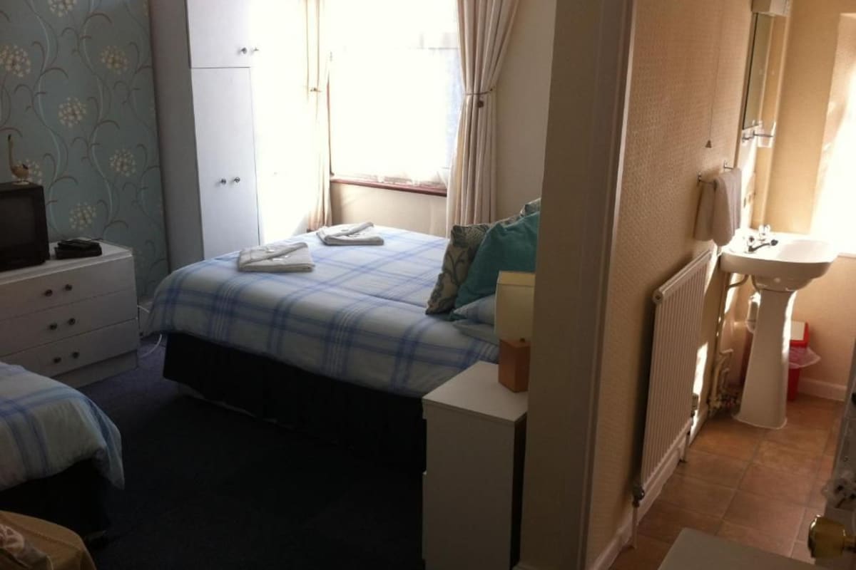 A bedroom with a bed, a dresser, a bedside table, and a window with curtains.