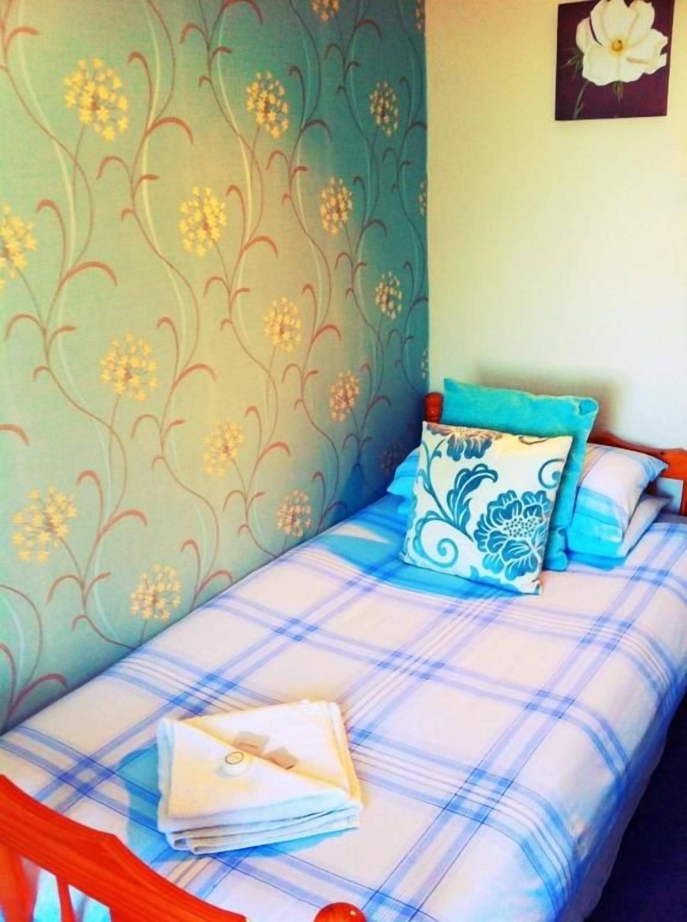 A single bed with a plaid bedspread, a blue and white pillow, and a folded white towel on the bed.