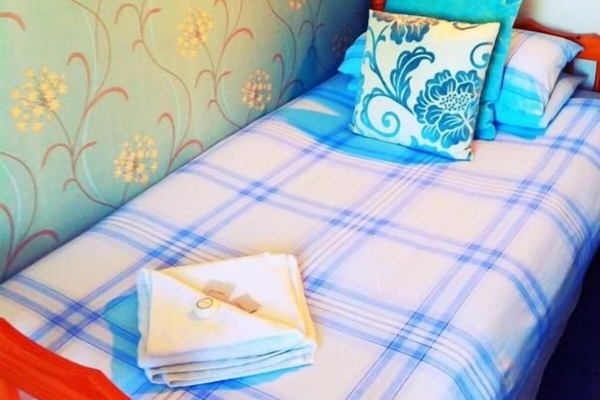A single bed with a plaid bedspread, a blue and white pillow, and a folded white towel on the bed.