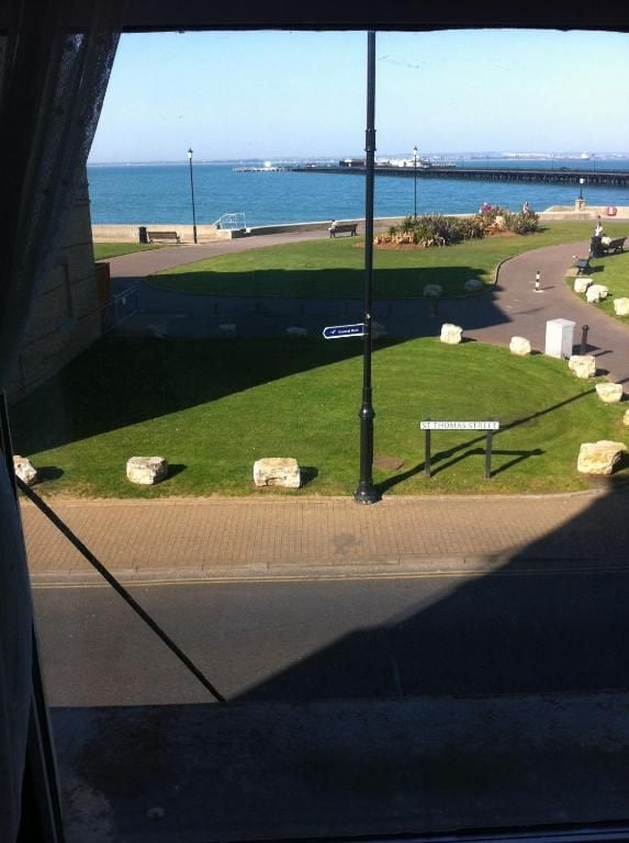 A view of a coastal area with a paved walkway, grassy areas, and a body of water in the background.