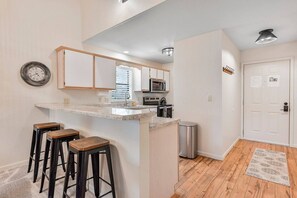 A modern kitchen with a central island, bar stools, a microwave, and a trash can. - The Golden Cricket -PointeRoyale (Branson)