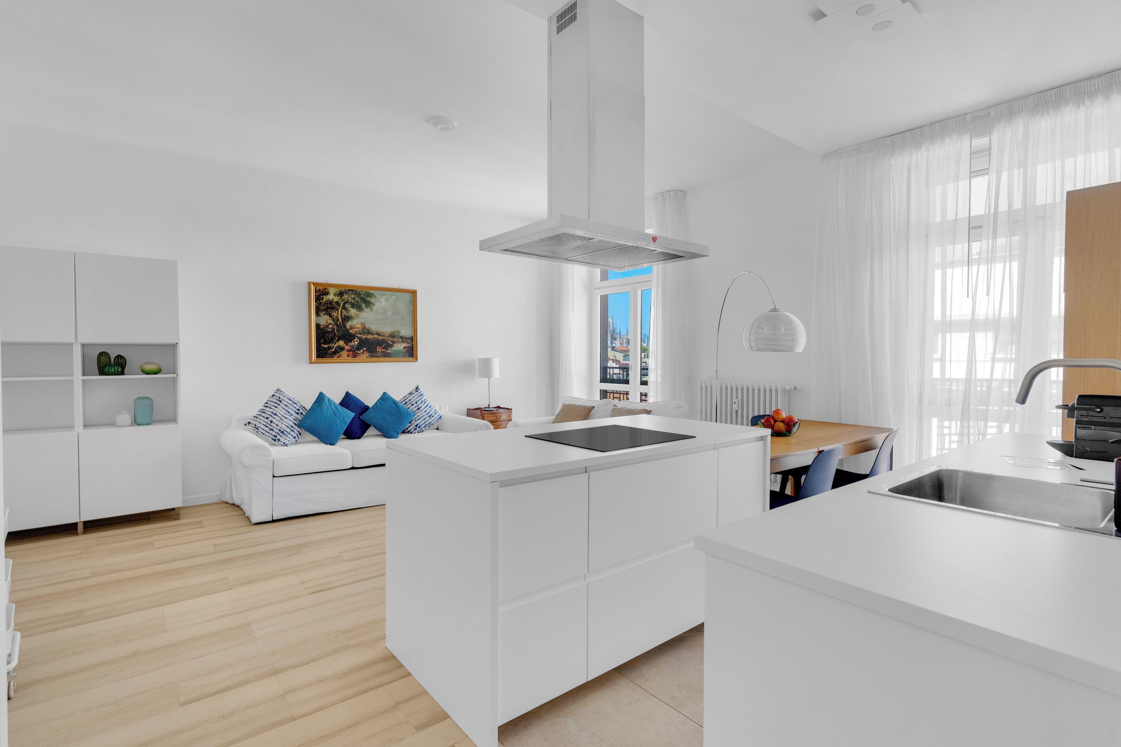 A modern kitchen with white cabinetry, a central island, and a view of the city through large windows.