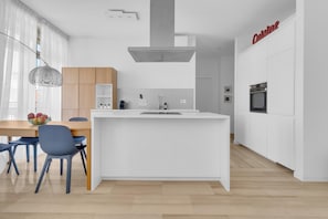 A modern kitchen with a central island, white cabinetry, and a dining area with blue chairs. - 4 Finestre sul duomo (Milan)