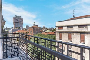 A balcony with a metal railing overlooking a cityscape with various buildings, including a church with a green dome and a tall modern building. - 4 Finestre sul duomo (Milan)