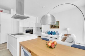 A modern kitchen with white cabinetry, a built-in stove, and a dining area with a wooden table and a fruit bowl. - 4 Finestre sul duomo (Milan)