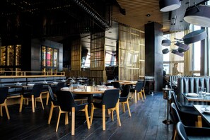 A restaurant interior with wooden tables and chairs, a bar area, and a high ceiling with hanging lights. - NovaStar Test Hotel 0l3aex (Sedalia)