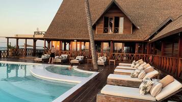 A wooden building with a pool, lounge chairs, and a palm tree.