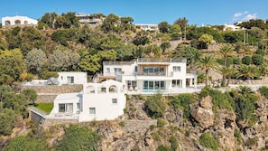 Ein modernes, mehrgeschossiges Haus mit Pool, umgeben von felsigem Gelände und Vegetation.
