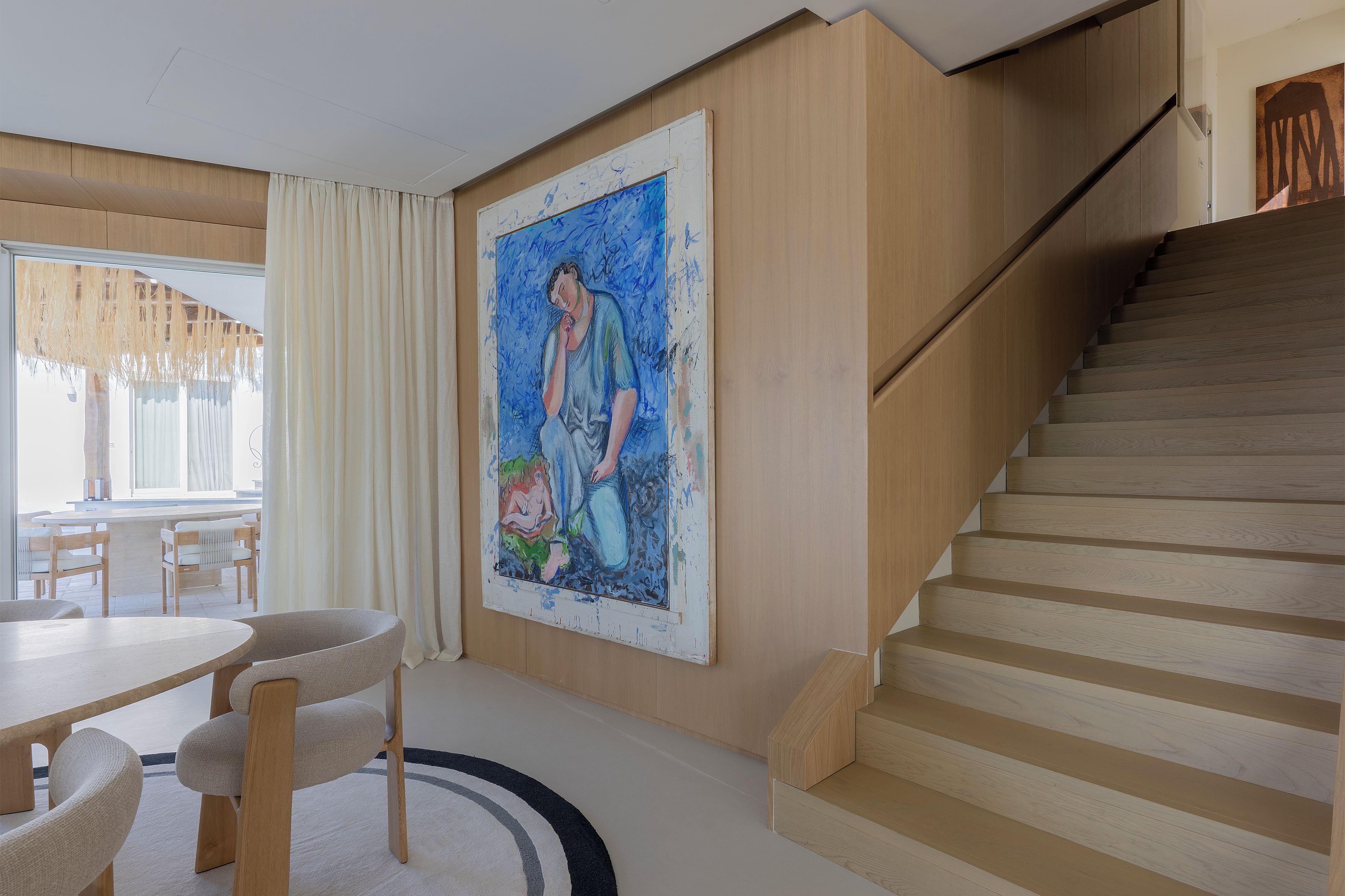 Un interior moderno con una escalera, una zona de comedor y un cuadro grande en la pared.