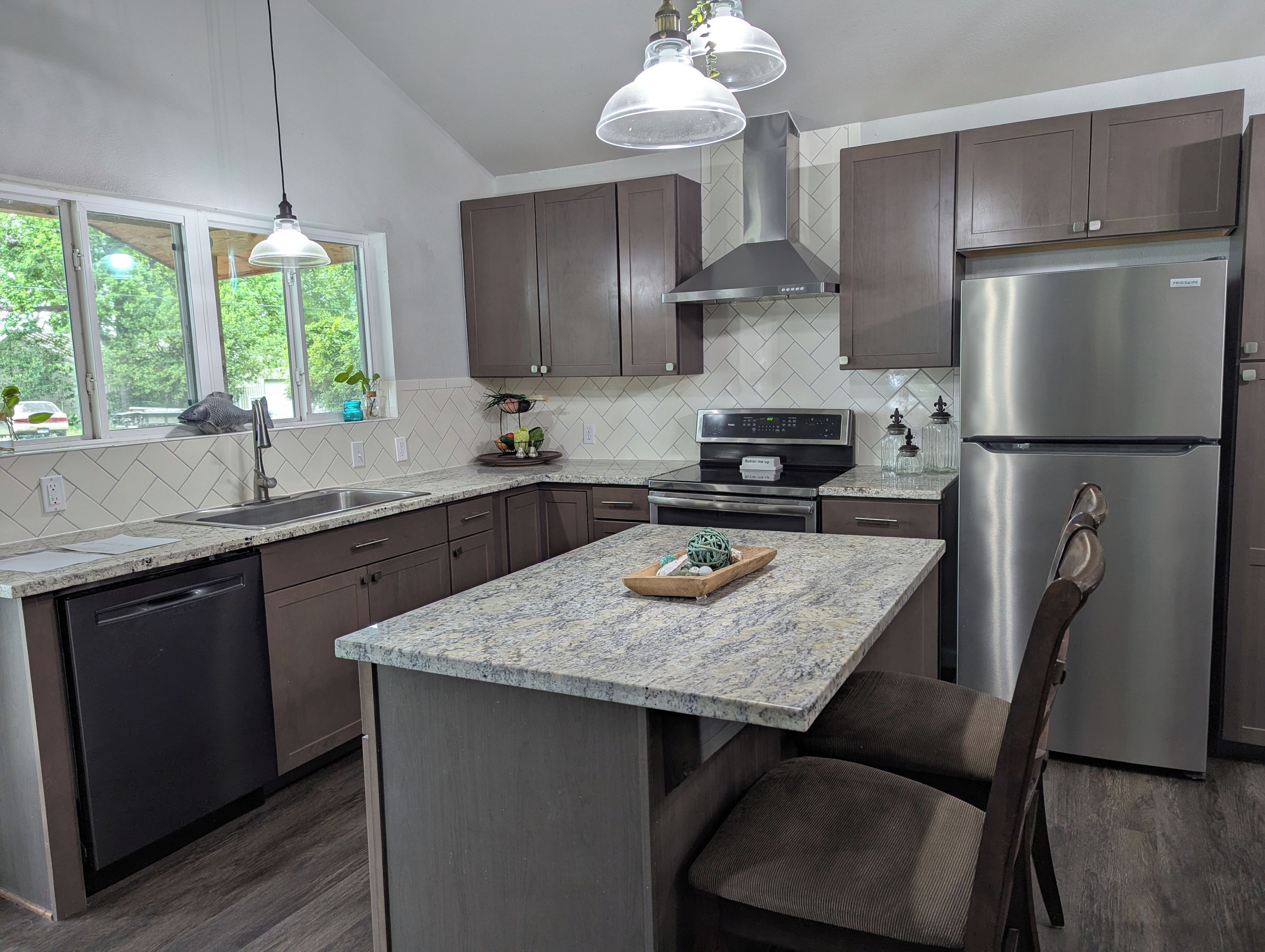 A modern kitchen with dark wood cabinets, a stainless steel refrigerator, and a granite countertop.