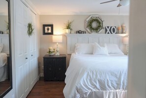 Een slaapkamer met een bed, een kaptafel, een spiegel en een wand met decoratieve objecten.