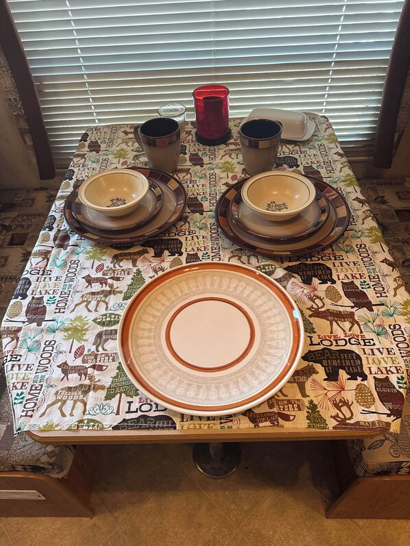 A dining table set with plates, bowls, and a red cup, covered by a tablecloth with wildlife prints.