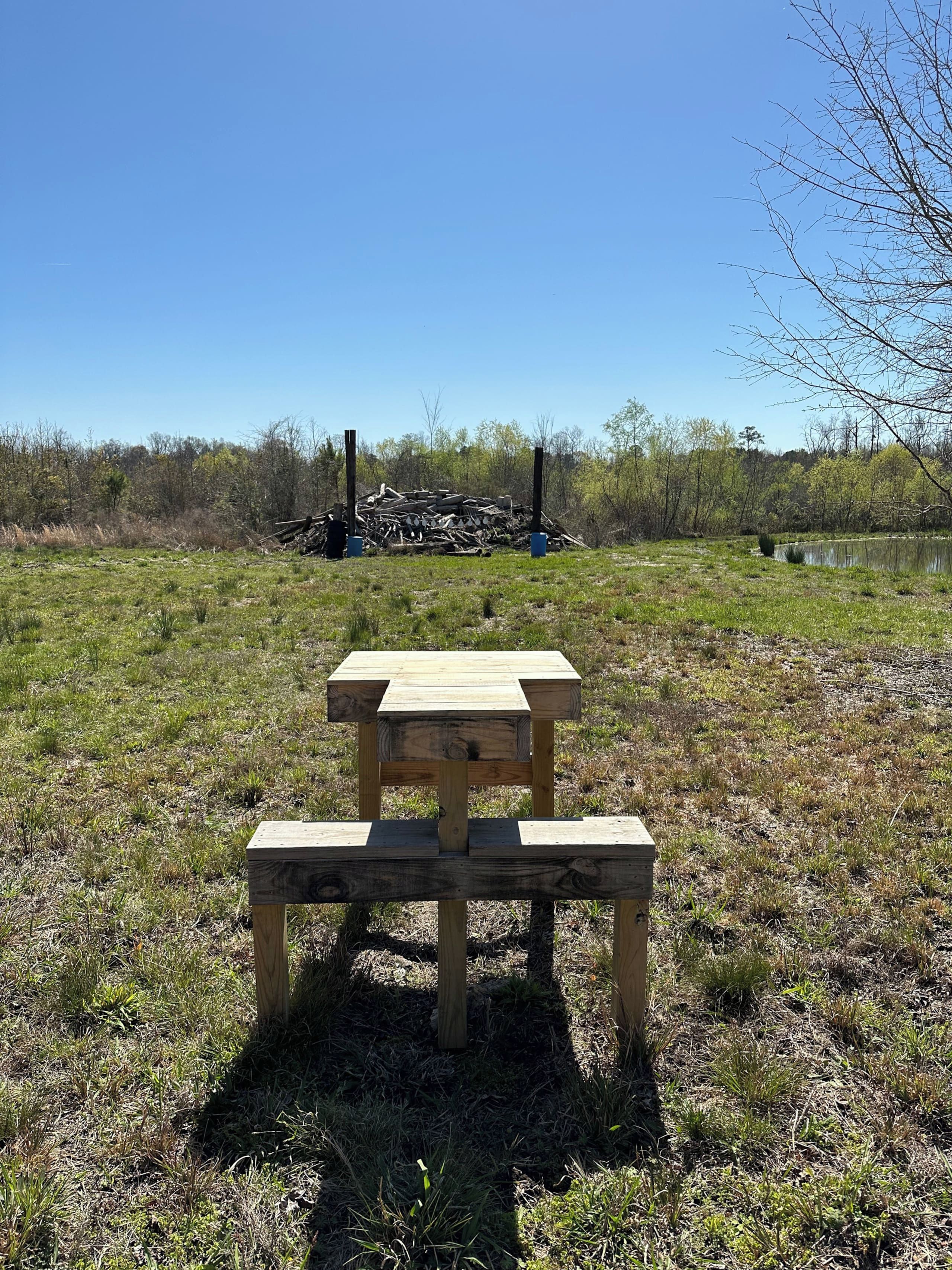 Ein Picknicktisch in einer grünen Wiese, im Hintergrund ein Holzstoß.