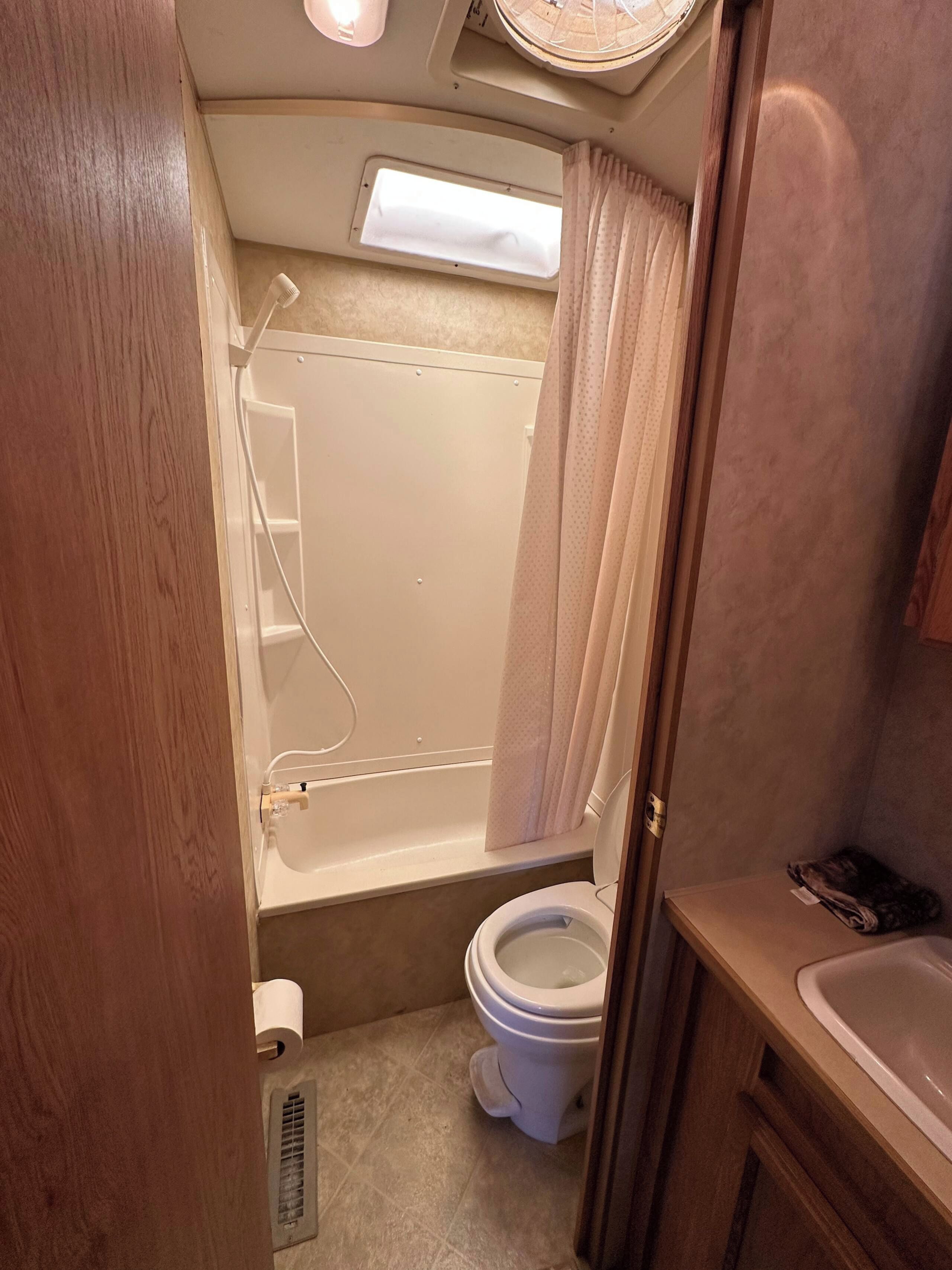 A compact bathroom with a bathtub, toilet, and a small window.