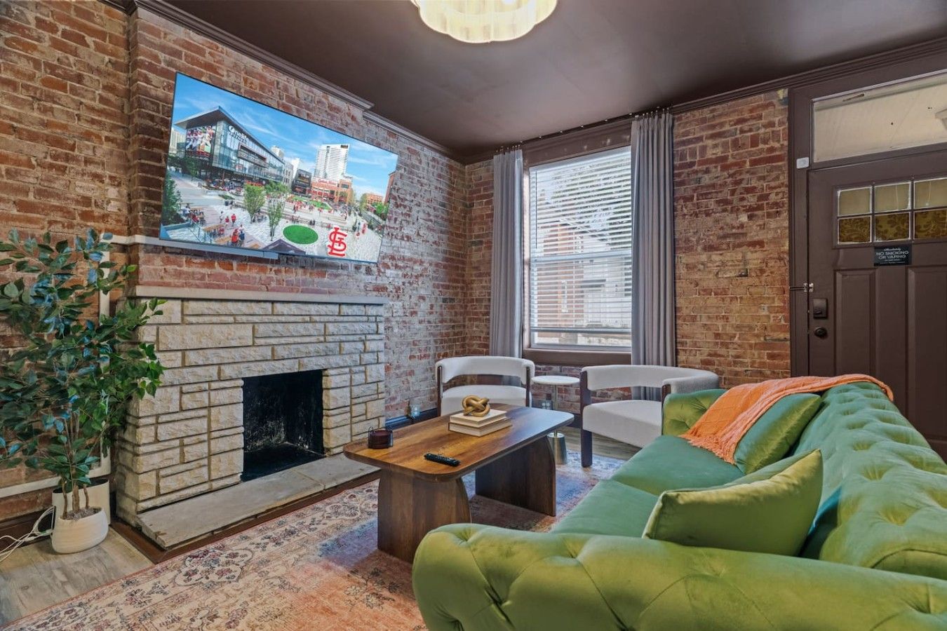A living room with a brick wall, a fireplace, a green sofa, a coffee table, and a television mounted on the wall.