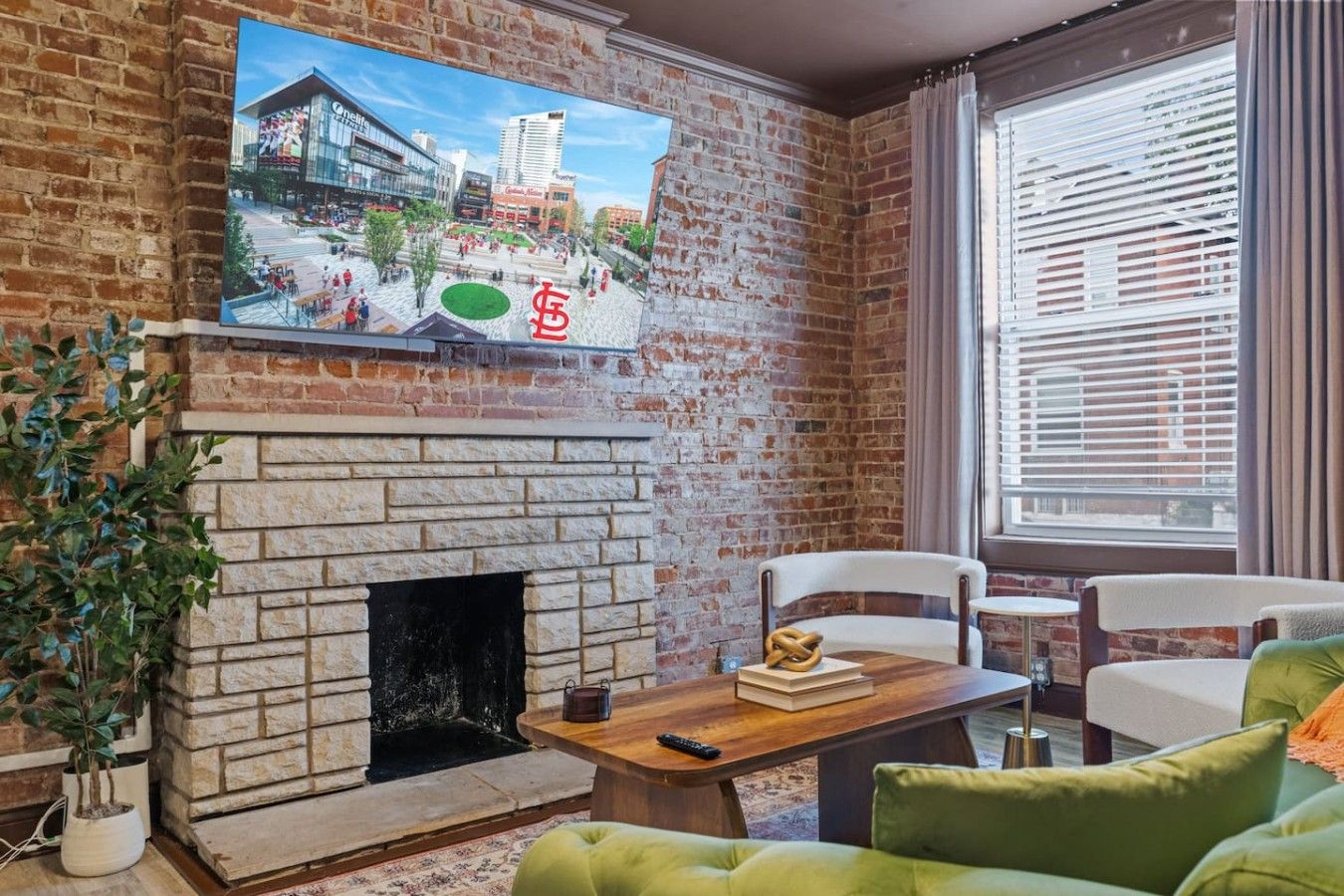 Een woonkamer met een metselwerk open haard, een aan de muur bevestigde televisie en een raam met luxaflex.