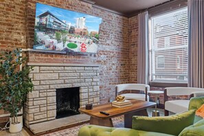 Una sala de estar con chimenea de ladrillo, televisor montado en la pared y ventana con persianas.