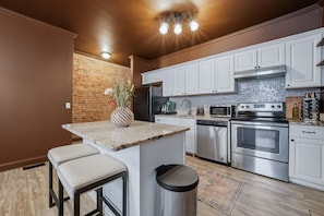 A kitchen with white cabinets, stainless steel appliances, a brick accent wall, and a small bar area with stools.