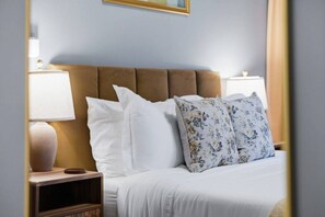 A hotel room with a bed, white bedding, a brown upholstered headboard, and two bedside lamps.