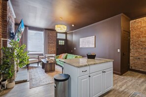 A modern kitchen with a central island, a dining area with a sofa and chairs, and a brick accent wall.