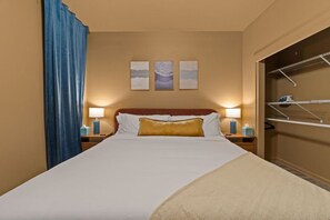 A hotel room with a bed, two bedside lamps, a blue curtain, and a closet with a hanging rack.