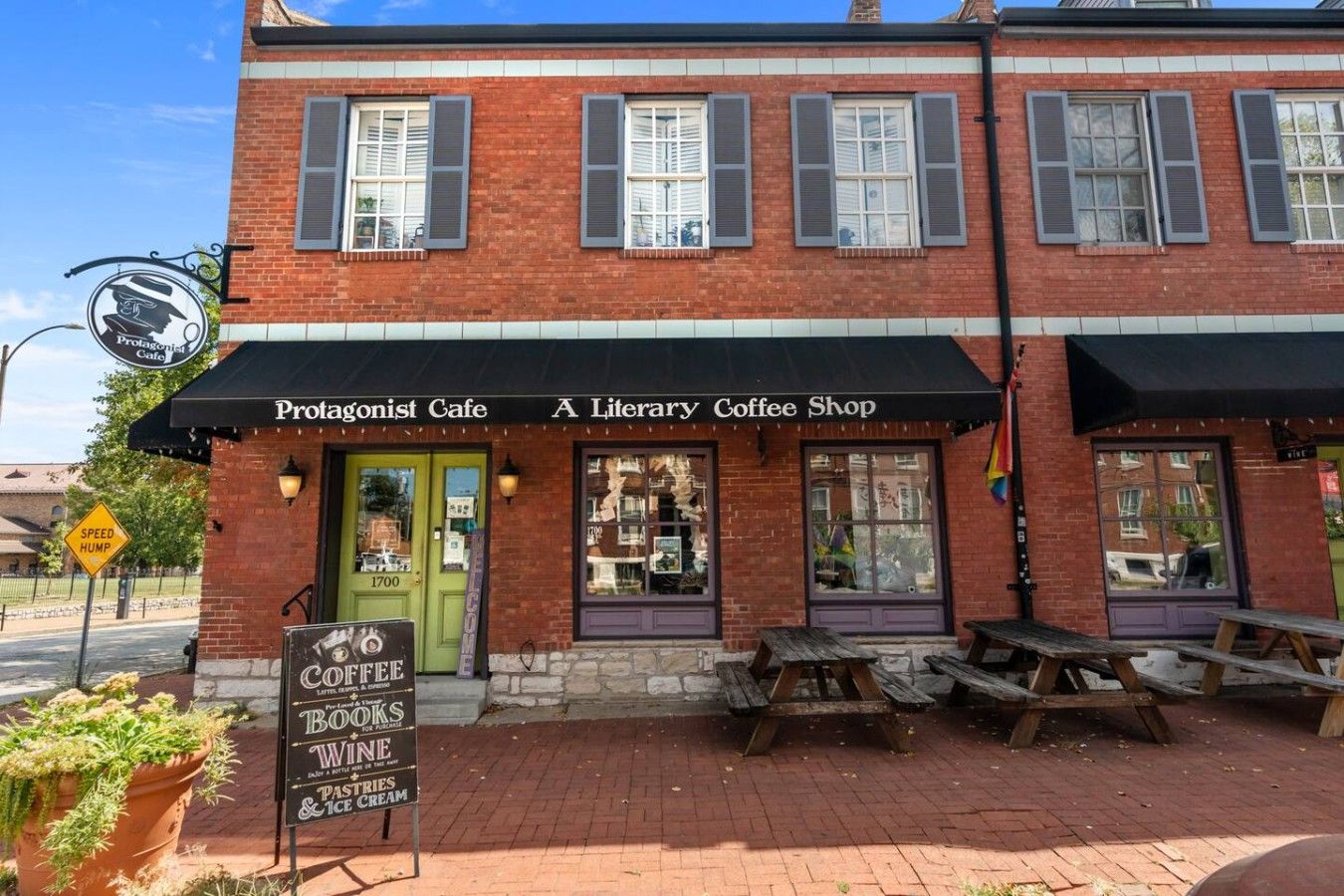 Un edificio de ladrillo con una puerta verde y un toldo negro con la leyenda 'Protagonist Cafe A Literary Coffee Shop'.