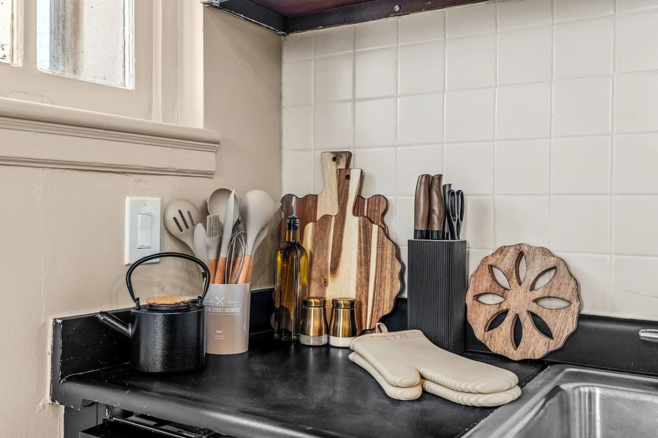 A kitchen counter with various utensils, a wooden cutting board, a knife block, and a decorative wooden piece.