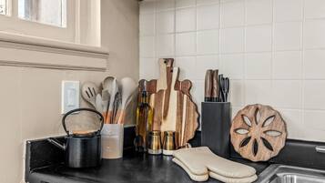 A kitchen counter with various utensils, a wooden cutting board, a knife block, and a decorative wooden piece.