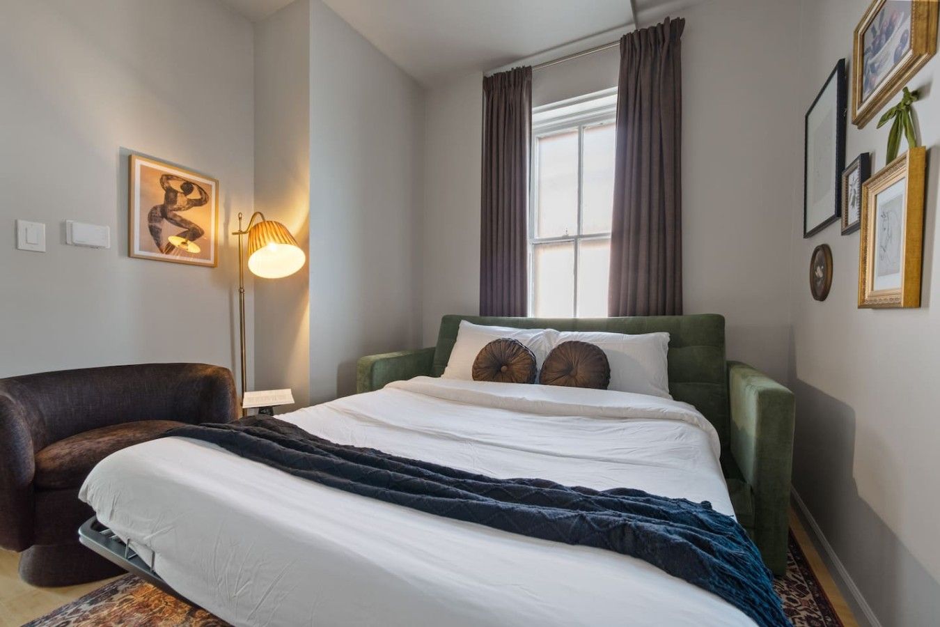 A hotel room with a bed, a chair, a lamp, and a window with curtains.
