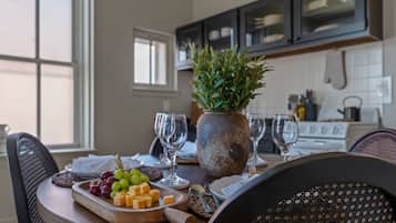 Una mesa de comedor con una tabla de quesos y uvas, una planta en maceta y copas de vino.