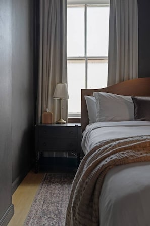 Una camera da letto con un letto, un comodino, una lampada e una finestra con tende.