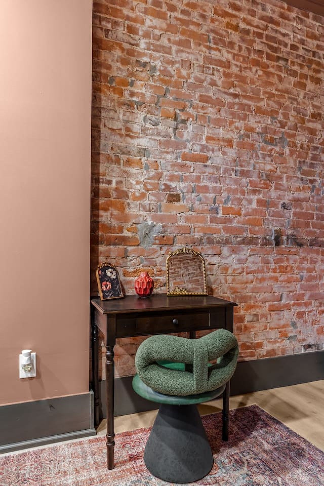 A room with a brick wall, a desk with a chair, and a decorative mirror.
