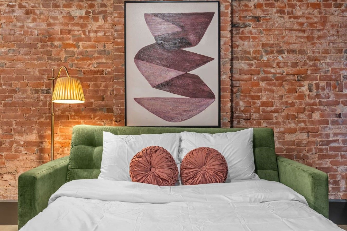 Una stanza con una testiera imbottita verde, biancheria da letto bianca e un quadro astratto appeso al muro.