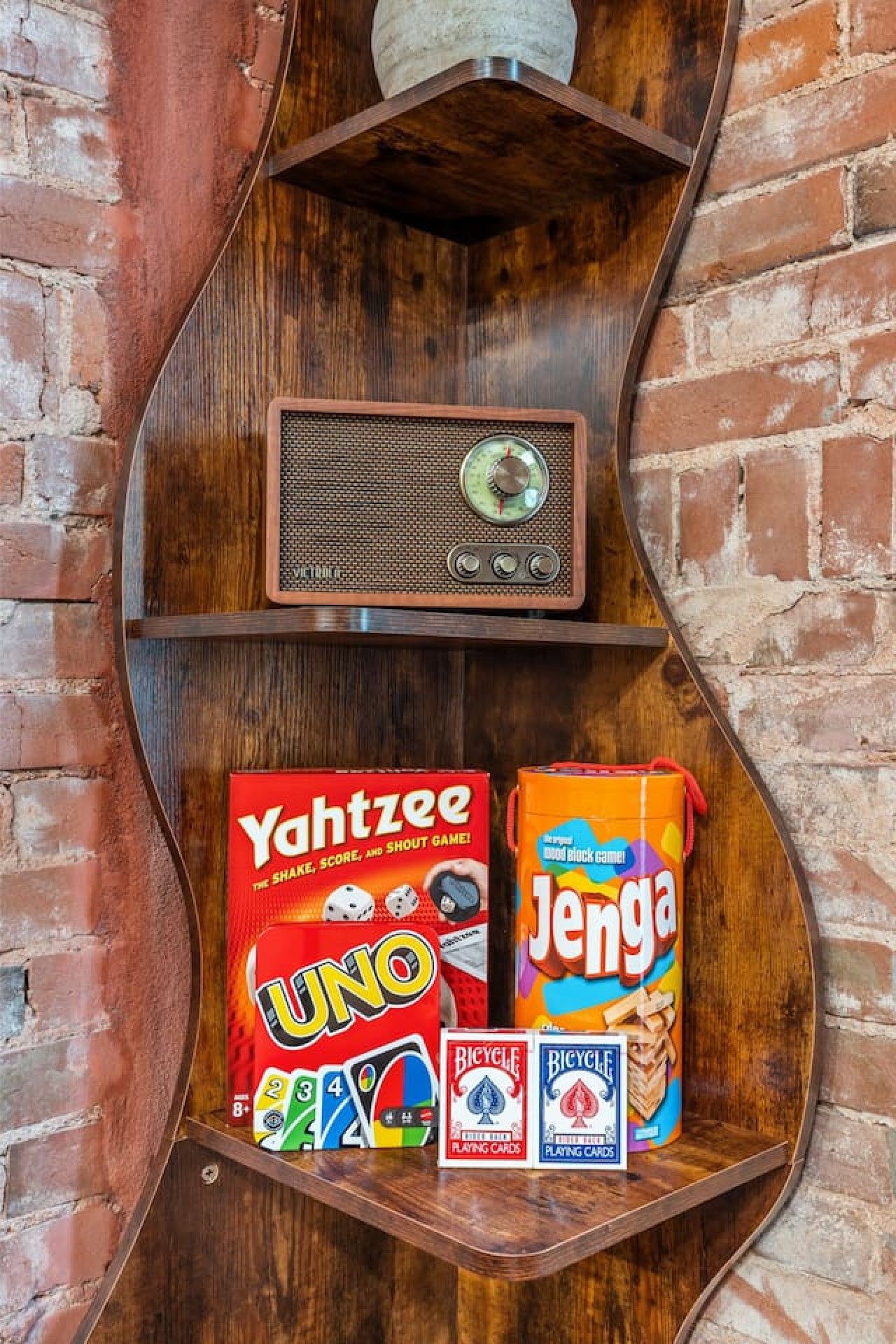 Un estante de madera con una radio antigua, un juego de Uno, una caja de Jenga y dos barajas de cartas.