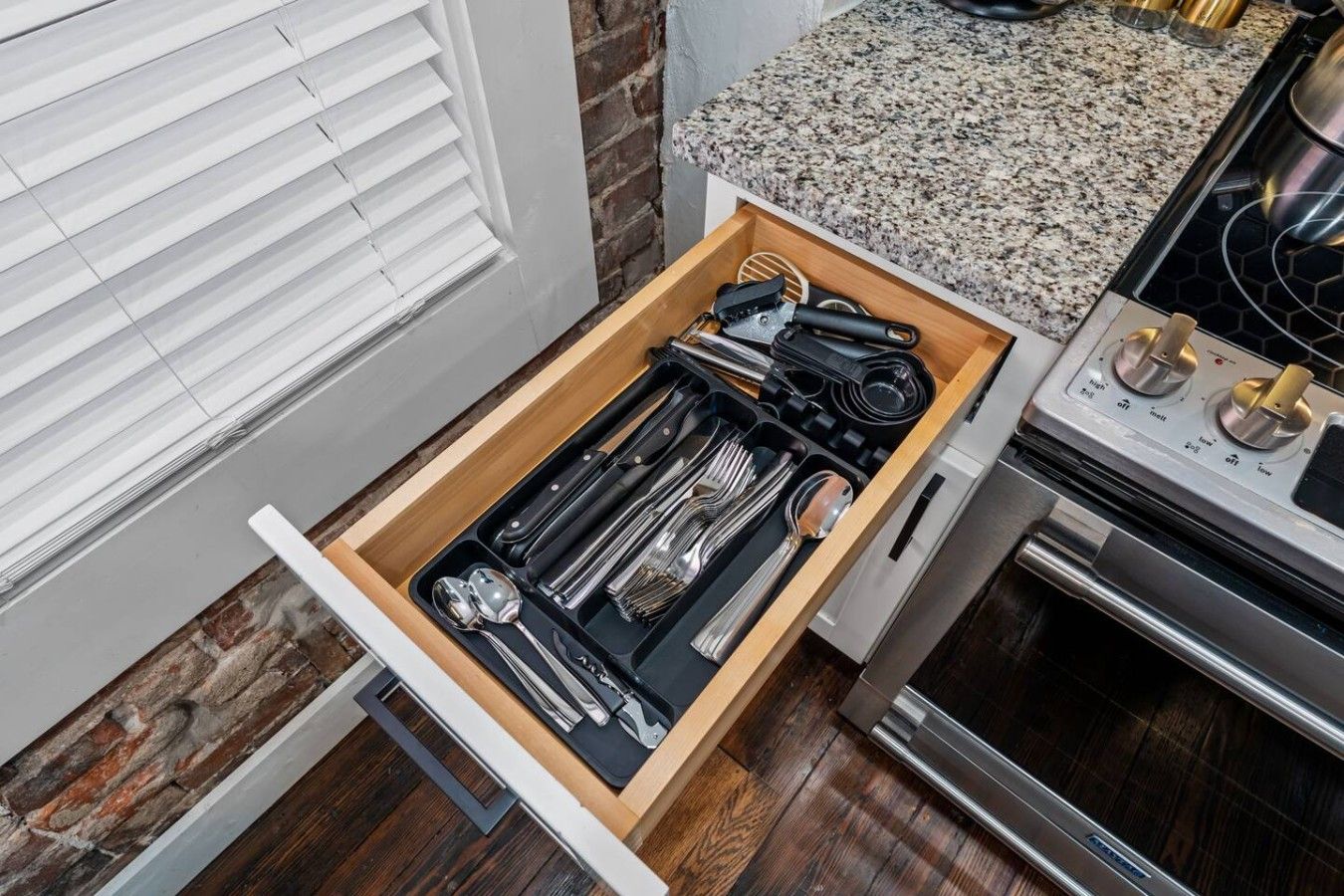 A kitchen with a drawer containing utensils and a stove.