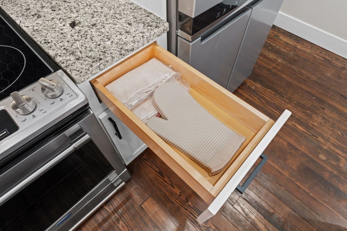 A kitchen with a granite countertop, stainless steel appliances, and a wooden drawer with a white interior.