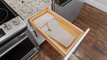 A kitchen with a granite countertop, stainless steel appliances, and a wooden drawer with a white interior.