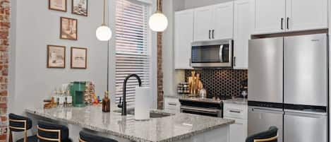 A modern kitchen with a central island, bar stools, stainless steel appliances, and pendant lighting.