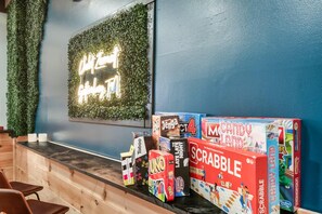 A hotel reception area with a blue wall, a green wall with a neon sign, and a counter with various board games. - Smoky Mtn Escape | Hot Tub • Fire Pit • Game Room (Gatlinburg)