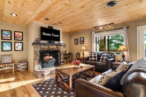 Ein gemütliches Wohnzimmer mit Kamin aus Stein, einer Ledersofa und einem darüber montierten Fernseher.