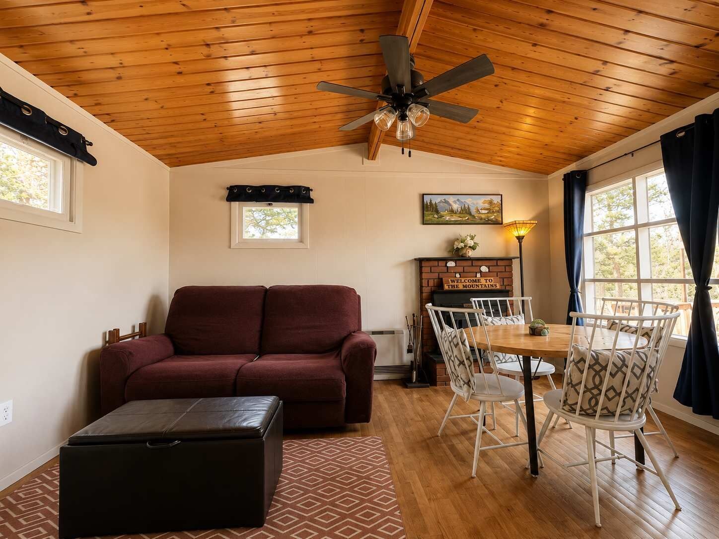 A cozy living room with a wooden ceiling, a sofa, a dining table with chairs, and a fireplace.
