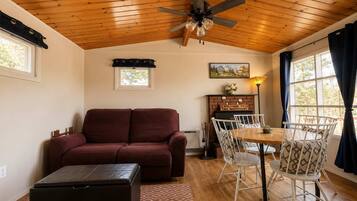A cozy living room with a wooden ceiling, a sofa, a dining table with chairs, and a fireplace.
