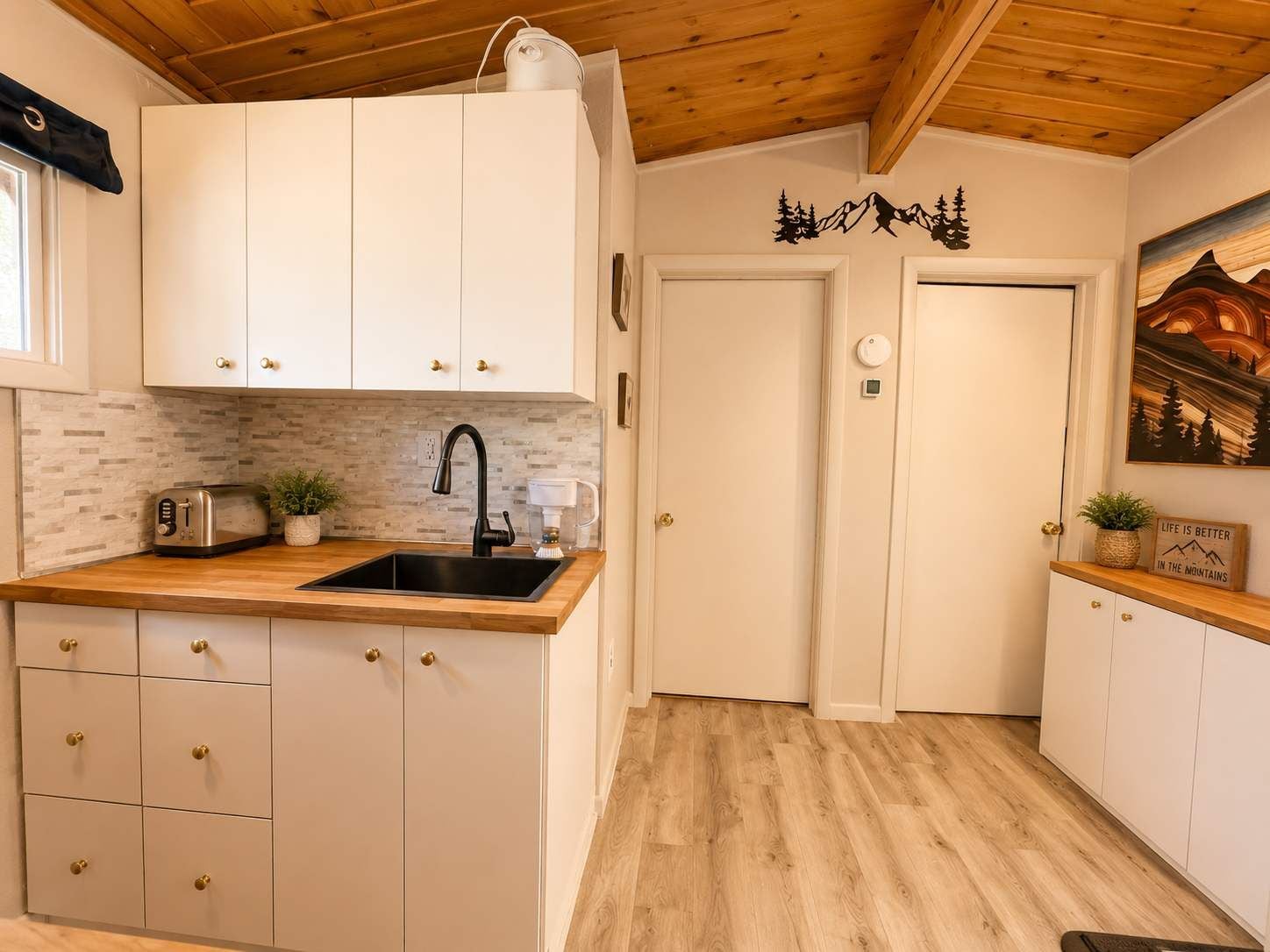 Ett kompakt kök med vita skåp, en träbänkskiva, en svart kran och en brödrost.