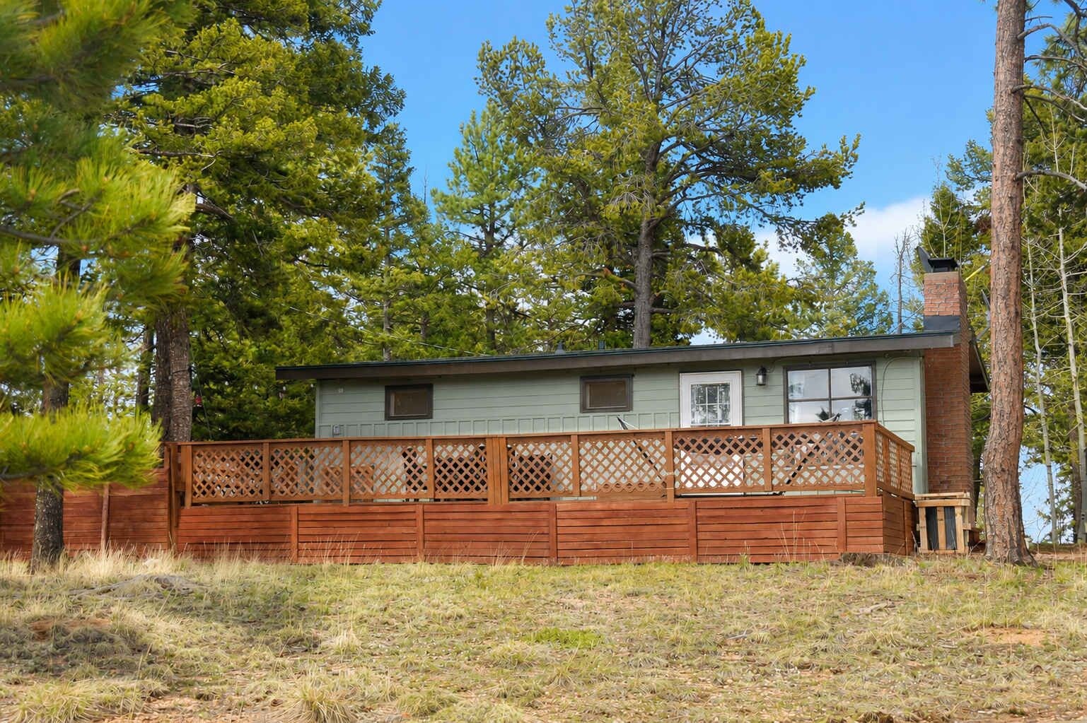 A single-story house with a wooden deck, surrounded by trees.