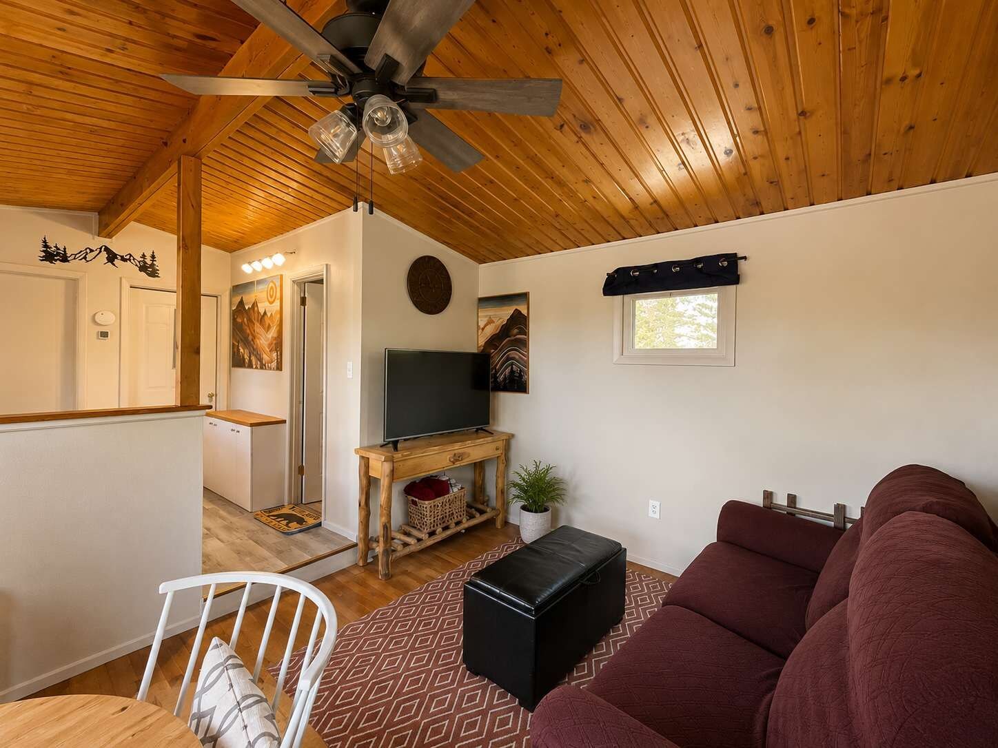 A cozy living room with a ceiling fan, a television, a red sofa, and a wooden dining table.