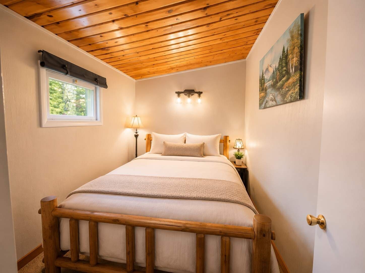 A bedroom with a wooden bed frame, a nightstand with a lamp, a painting on the wall, and a window with a view of greenery.