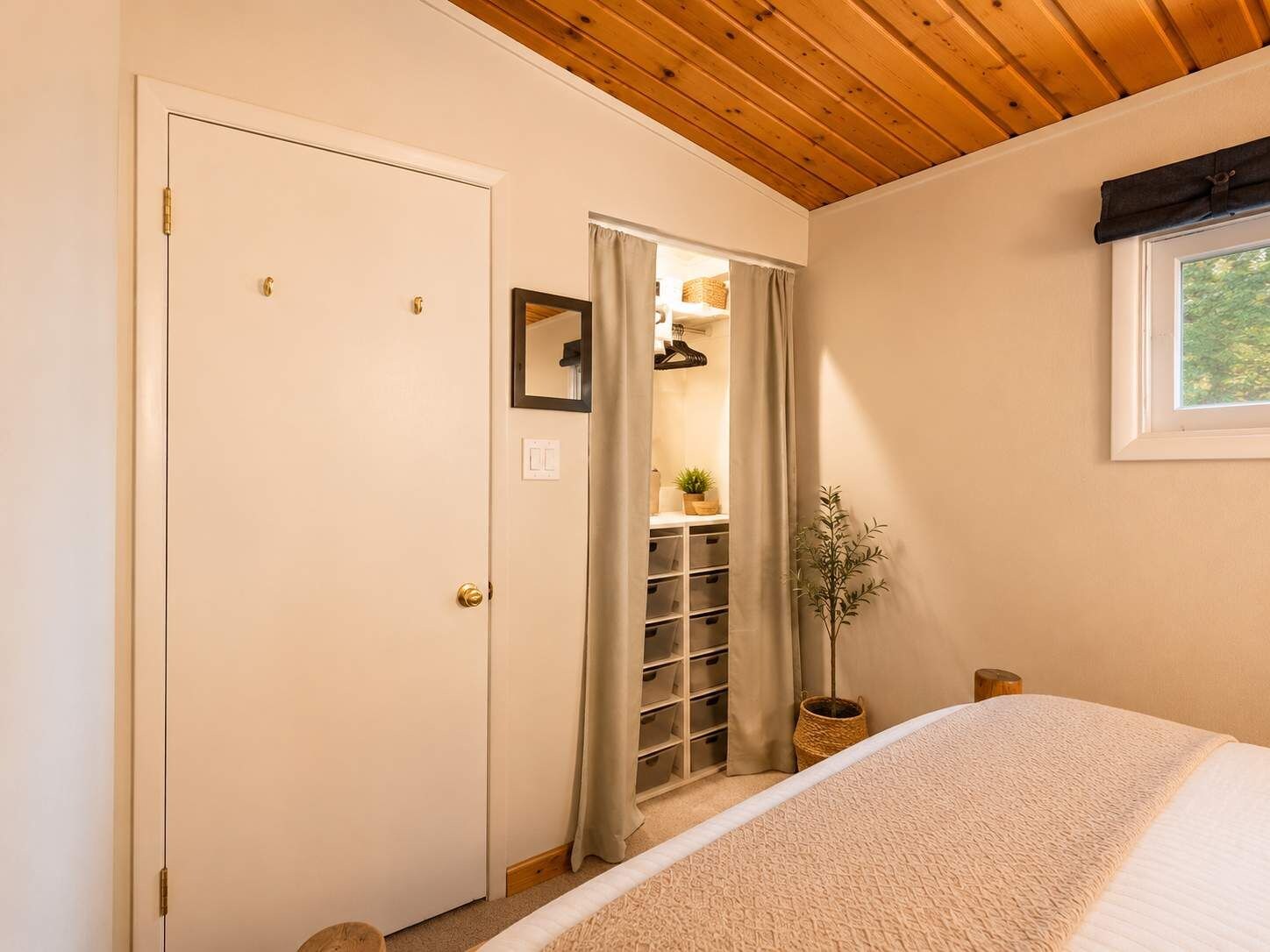 A bedroom with a bed, a wooden ceiling, a closet with shelves, and a window.