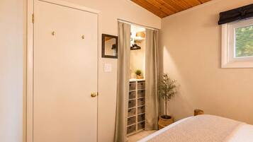 A bedroom with a bed, a wooden ceiling, a closet with shelves, and a window.
